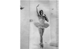 A ballerina in toe shoes and a tutu holds one arm above her head. 